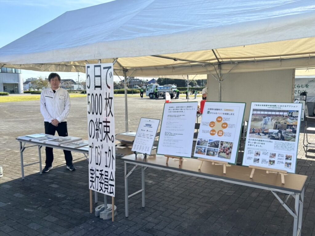 「5日で5000枚の約束。プロジェクト実行委員会」のブース。看板とパネルを並べた